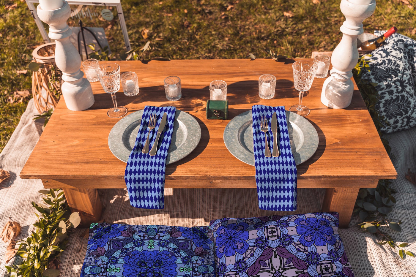 Outdoor dining setup with patterned textiles on a wooden table, decorative glassware, and rustic accents.