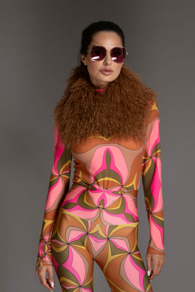 Person wearing a patterned outfit with fur collar and sunglasses on a gray background