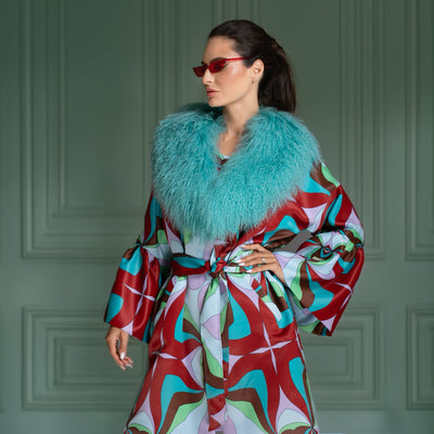 Woman wearing a colorful robe with a turquoise fur stole against a green paneled wall.